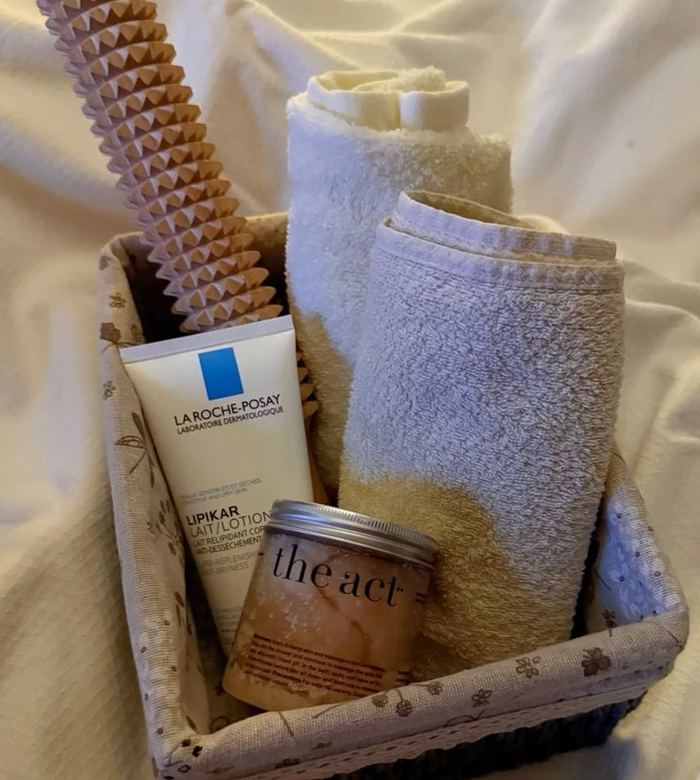 Basket of clean towels, body lotion and a scrub beside fresh linen
