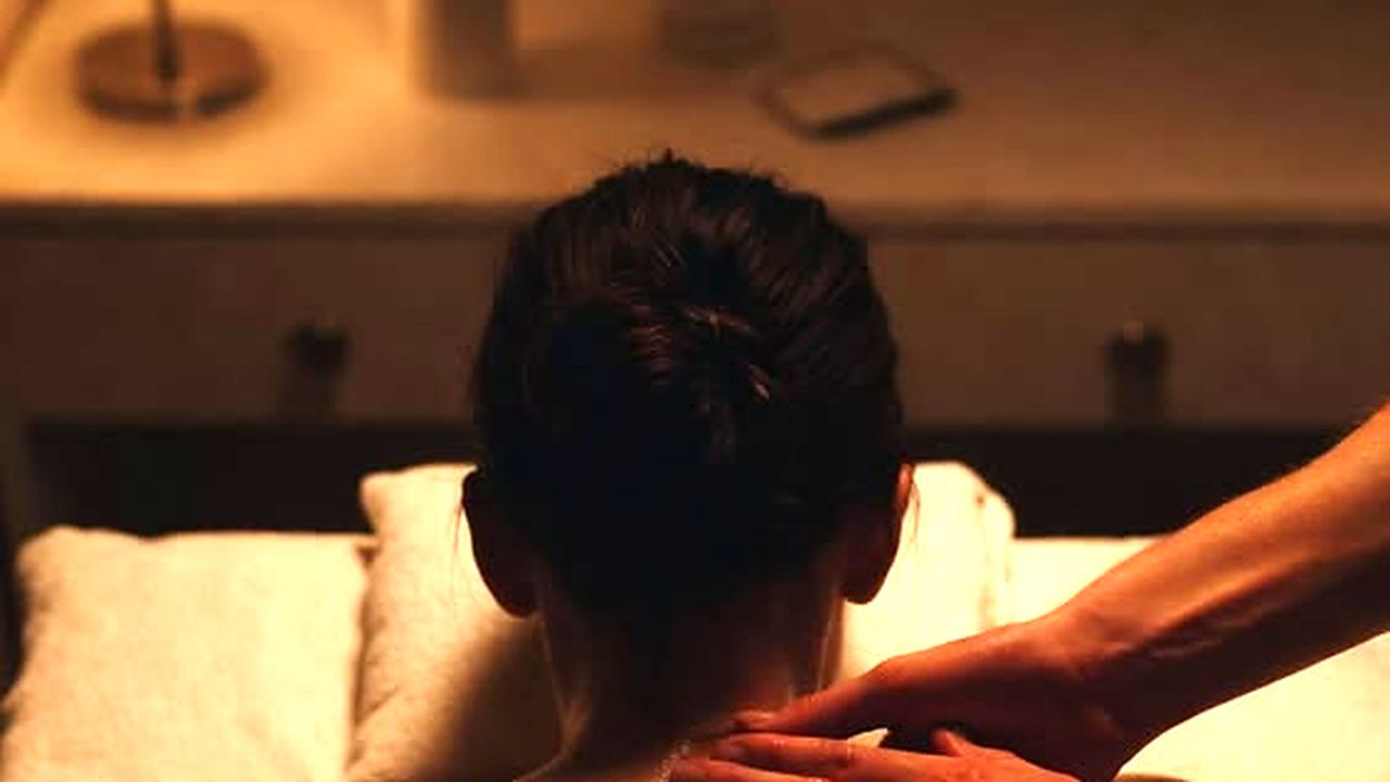 Therapist massaging a client's shoulders by candlelight in a darkened treatment room